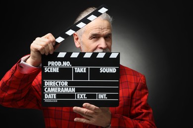Senior actor with clapperboard on black background. Film industry