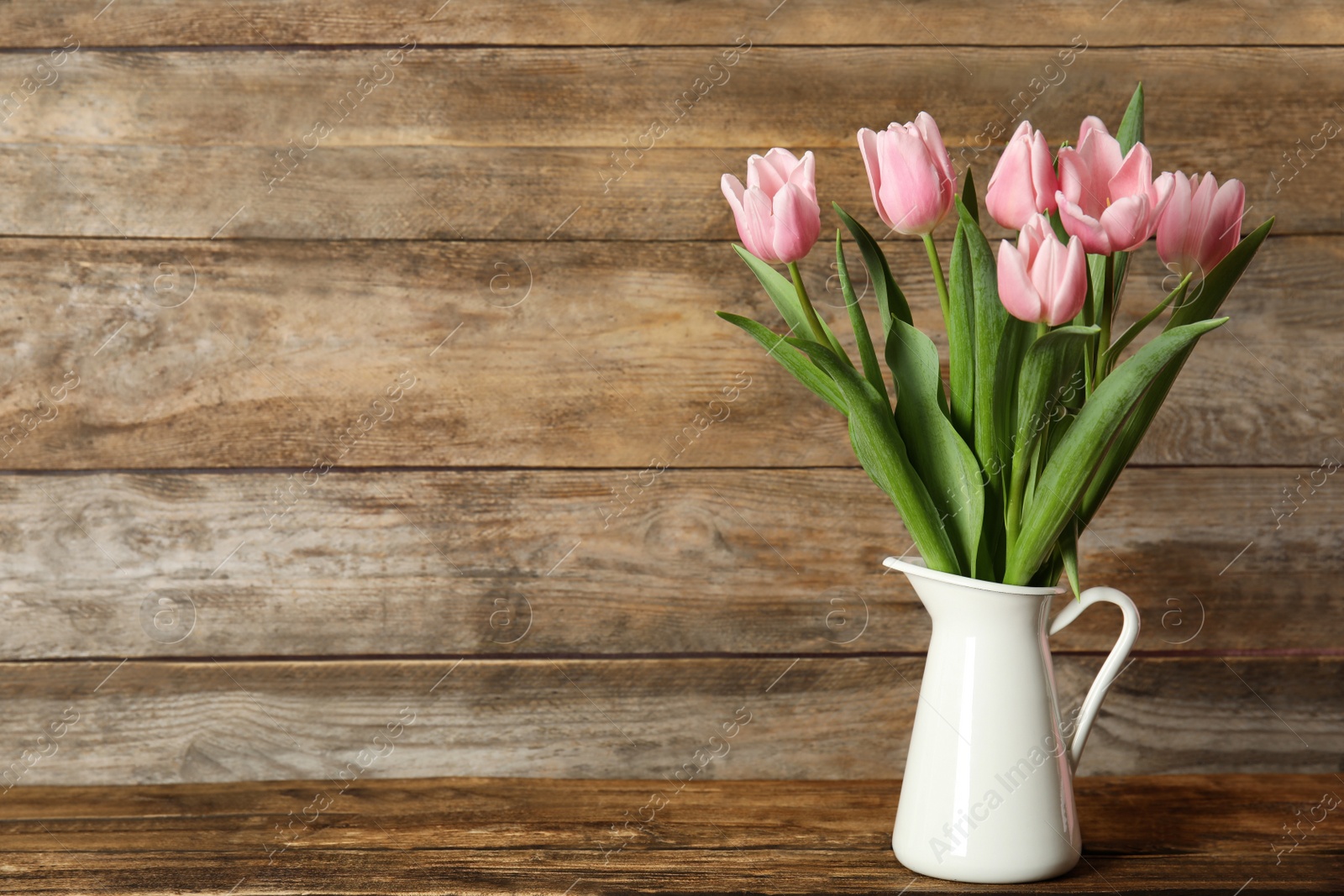Photo of Beautiful pink spring tulips in vase on wooden table. Space for text
