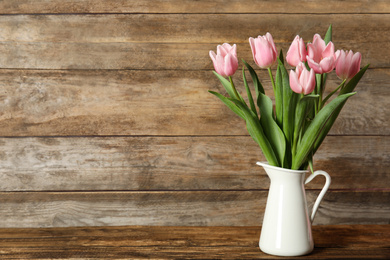 Beautiful pink spring tulips in vase on wooden table. Space for text