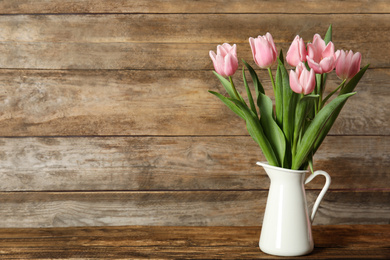 Photo of Beautiful pink spring tulips in vase on wooden table. Space for text