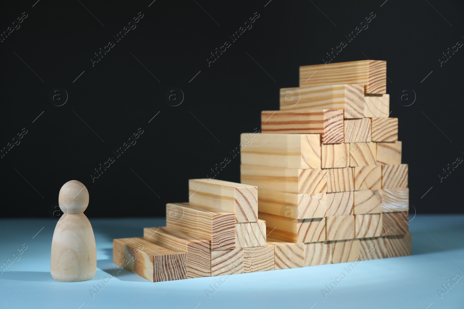 Photo of Stairs of blocks with gap as barrier and wooden human figure on light blue surface. Path to growth and success