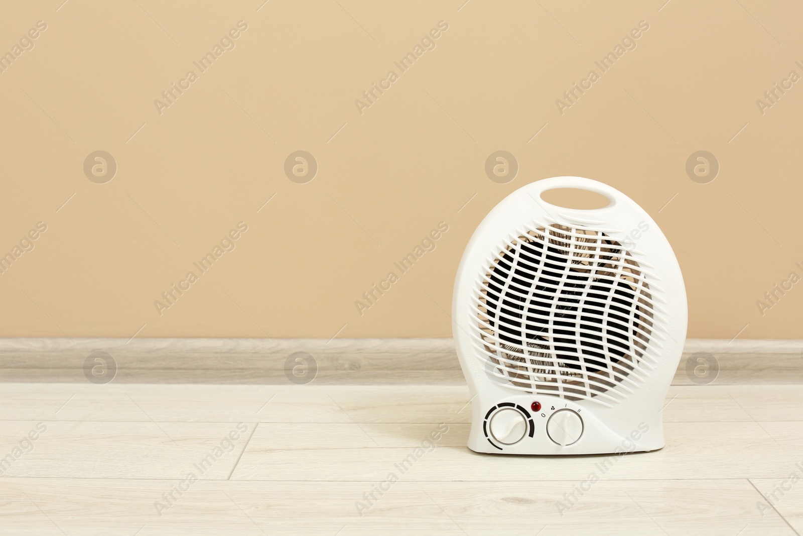 Photo of Modern electric fan heater on floor near beige wall, space for text