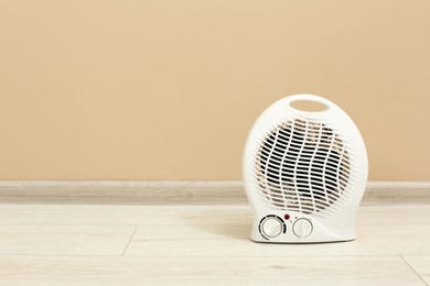 Photo of Modern electric fan heater on floor near beige wall, space for text