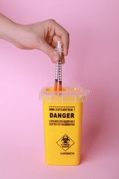 Photo of Woman throwing used syringes into sharps container  on pink background, closeup