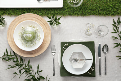 Elegant table setting with green plants on light cloth, flat lay