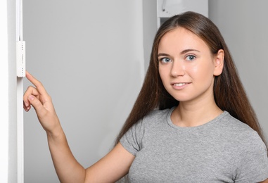 Photo of Woman adjusting thermostat on white wall. Heating system