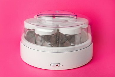 Photo of Modern yogurt maker with empty jars on pink background