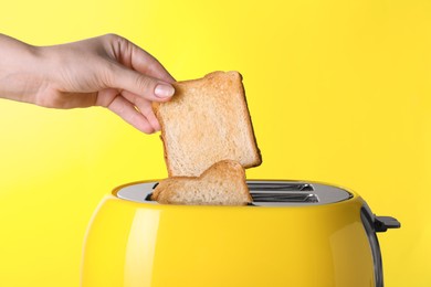 Photo of Woman taking roasted bread out of toaster on yellow background, closeup