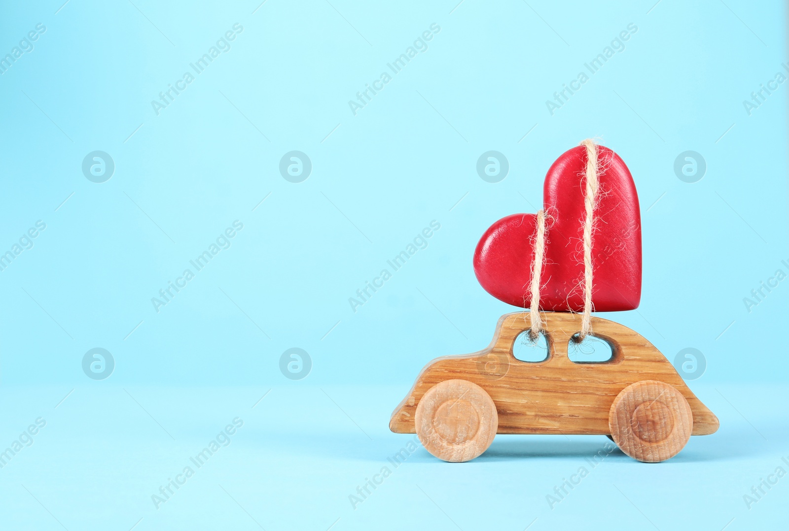 Photo of Red decorative heart tied to wooden toy car on color background. Space for text