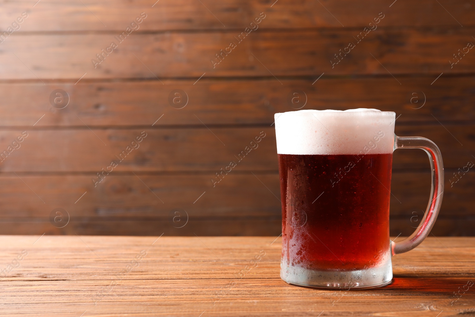 Photo of Glass mug with cold red beer on wooden table