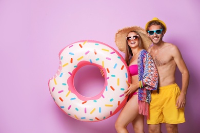 Photo of Young couple in beachwear with inflatable ring on color background