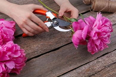 Photo of Woman trimming beautiful pink peonies with secateurs at wooden table, closeup