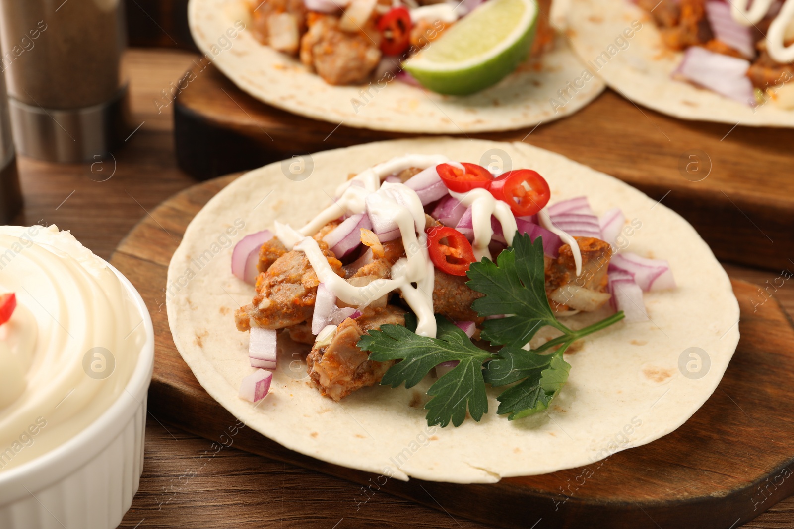 Photo of Delicious tacos with vegetables, meat and sauce on wooden table