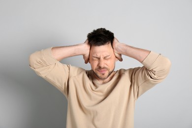 Man suffering from terrible migraine on light grey background