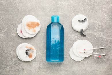 Photo of Dirty cotton pads, swabs and makeup removal product on grey table, flat lay