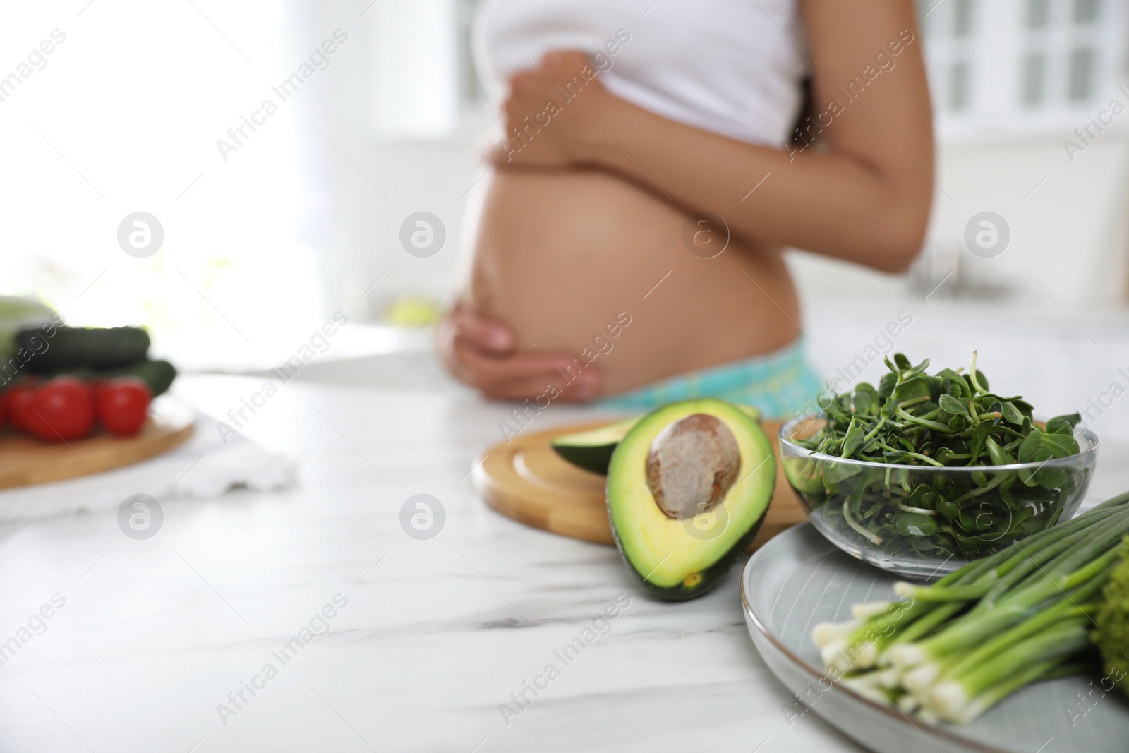 Photo of Fresh vegetables at table and young pregnant woman in kitchen, closeup. Taking care of baby health