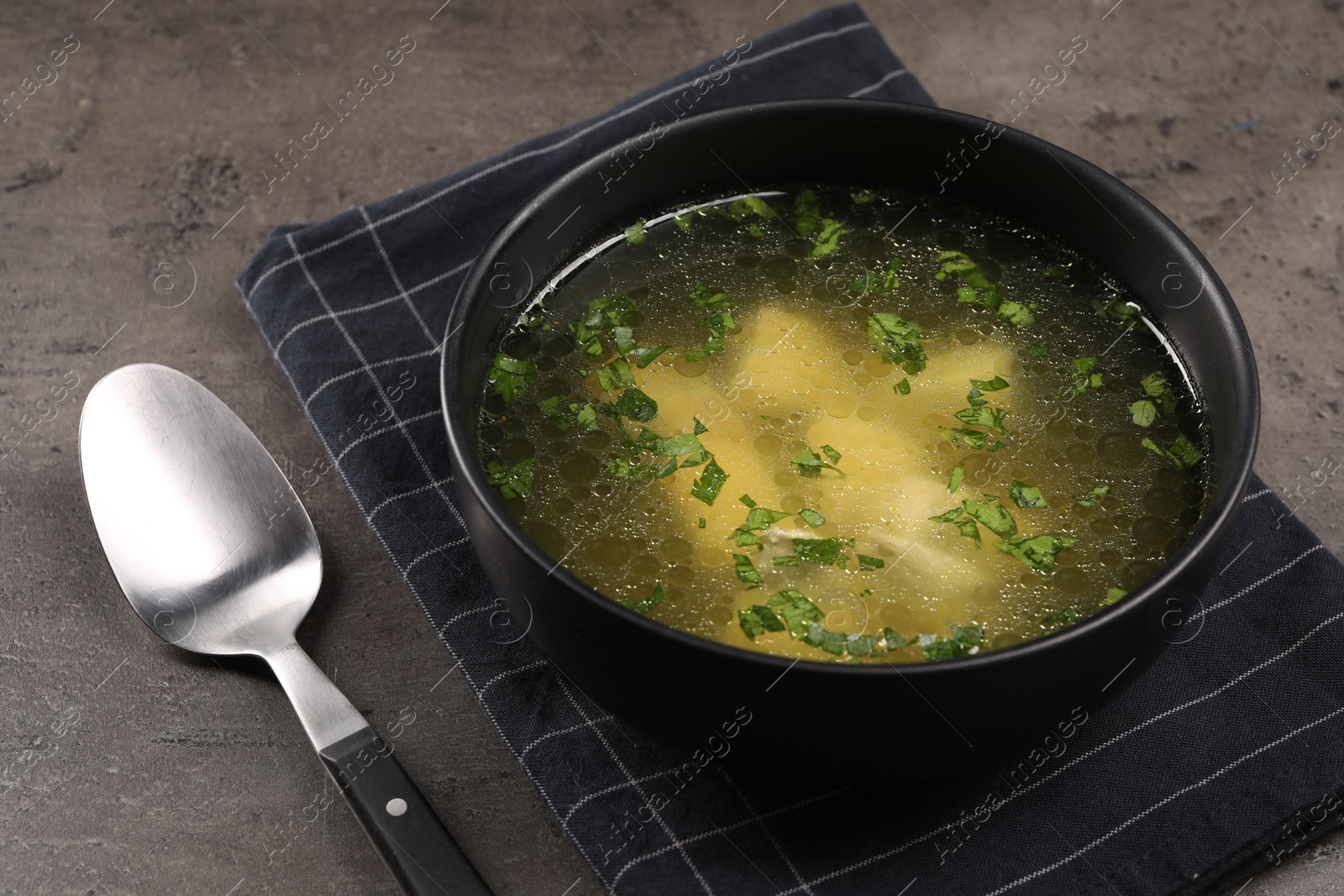 Photo of Delicious chicken soup with parsley and spoon on grey table, closeup
