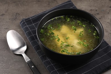 Photo of Delicious chicken soup with parsley and spoon on grey table, closeup