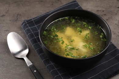 Delicious chicken soup with parsley and spoon on grey table, closeup