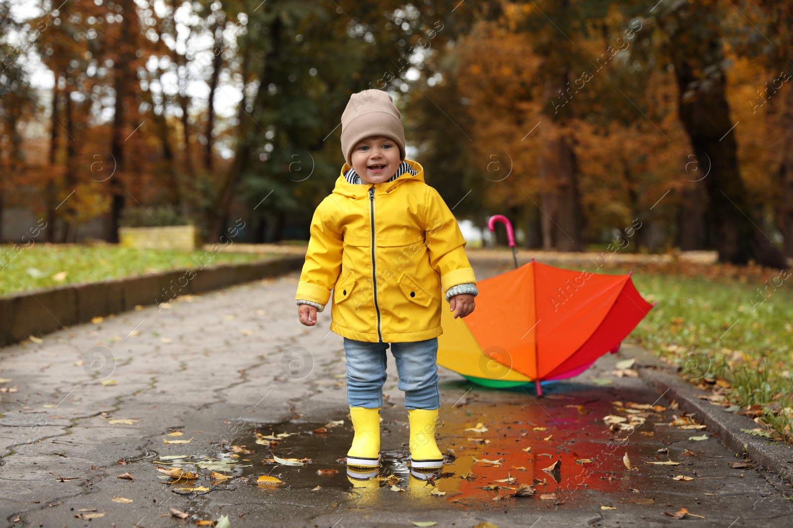 Photo of Cute little girl standing in puddle near colorful umbrella outdoors