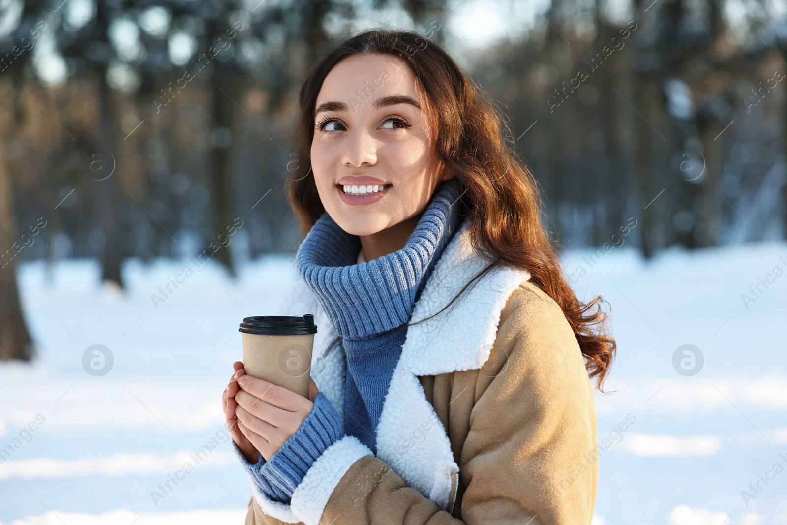 Photo of Portrait of smiling woman with paper cup of coffee in snowy park