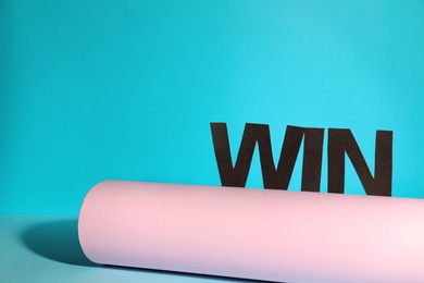 Photo of Rolled paper with word WIN on color background, space for text. Victory concept