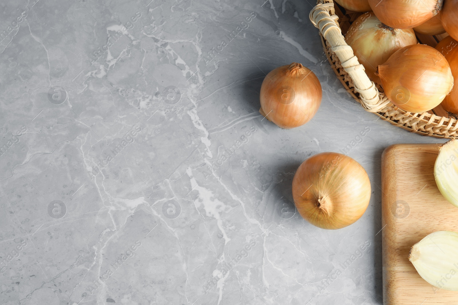 Photo of Flat lay composition with ripe onions, wooden board and basket on grey background, space for text