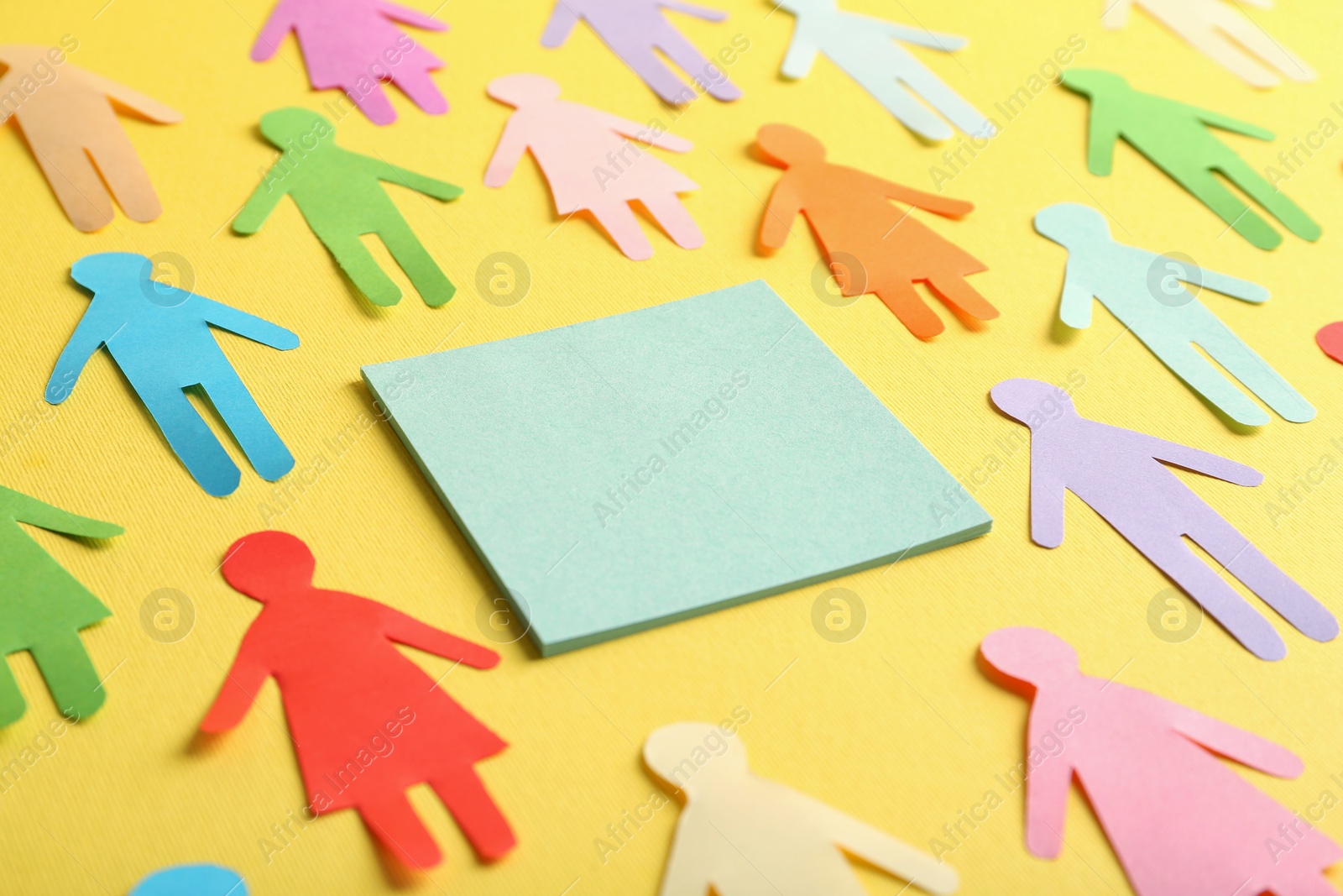 Photo of Many different paper human figures around blank card on yellow background, space for text. Diversity and inclusion concept