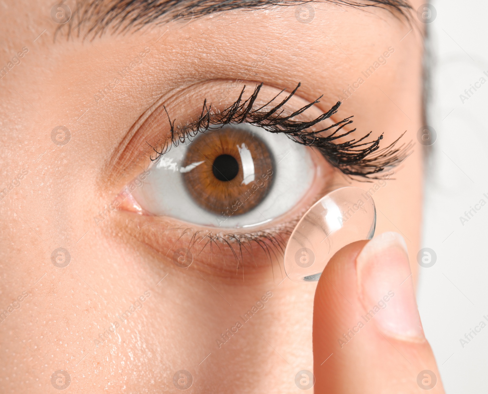 Photo of Young woman putting contact lens in her eye, closeup