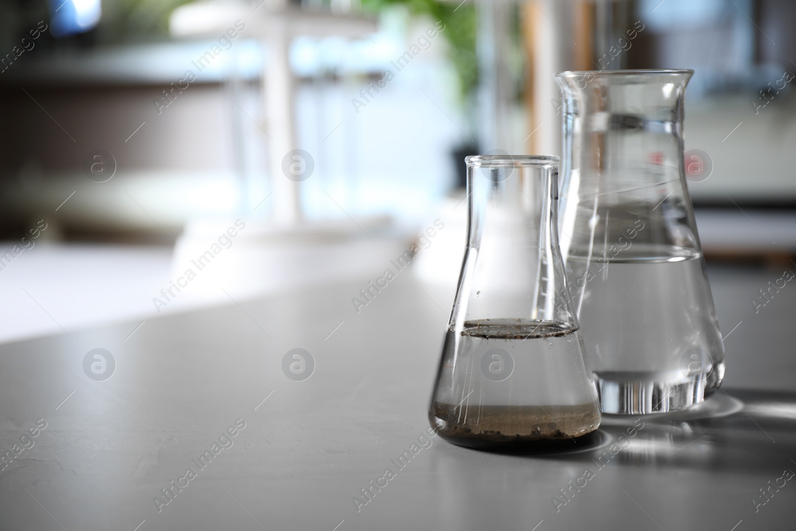 Photo of Glassware with soil extract and water on grey table, space for text. Laboratory research