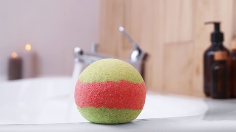 Photo of Colorful bath bomb on white tub in bathroom