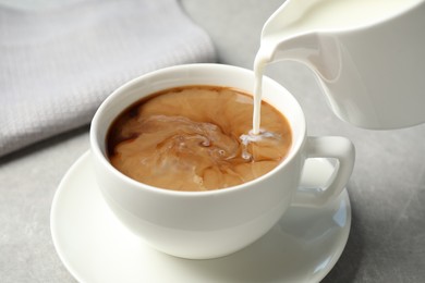 Photo of Pouring milk into cup of hot coffee on grey table, closeup