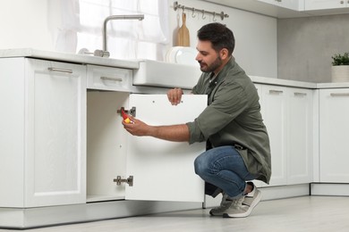 Photo of Man with screwdriver assembling furniture in kitchen