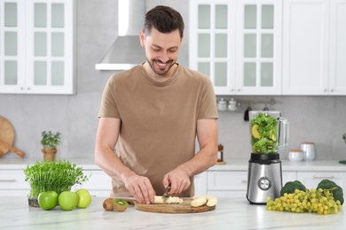 Photo of Happy man cutting bananas for delicious smoothie at white marble table in kitchen