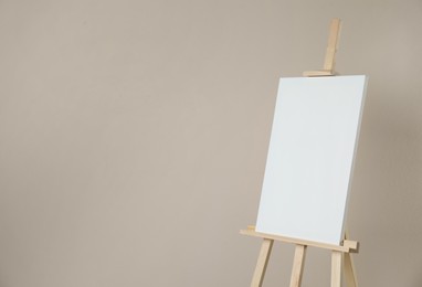 Photo of Wooden easel with blank canvas on beige background. Space for text