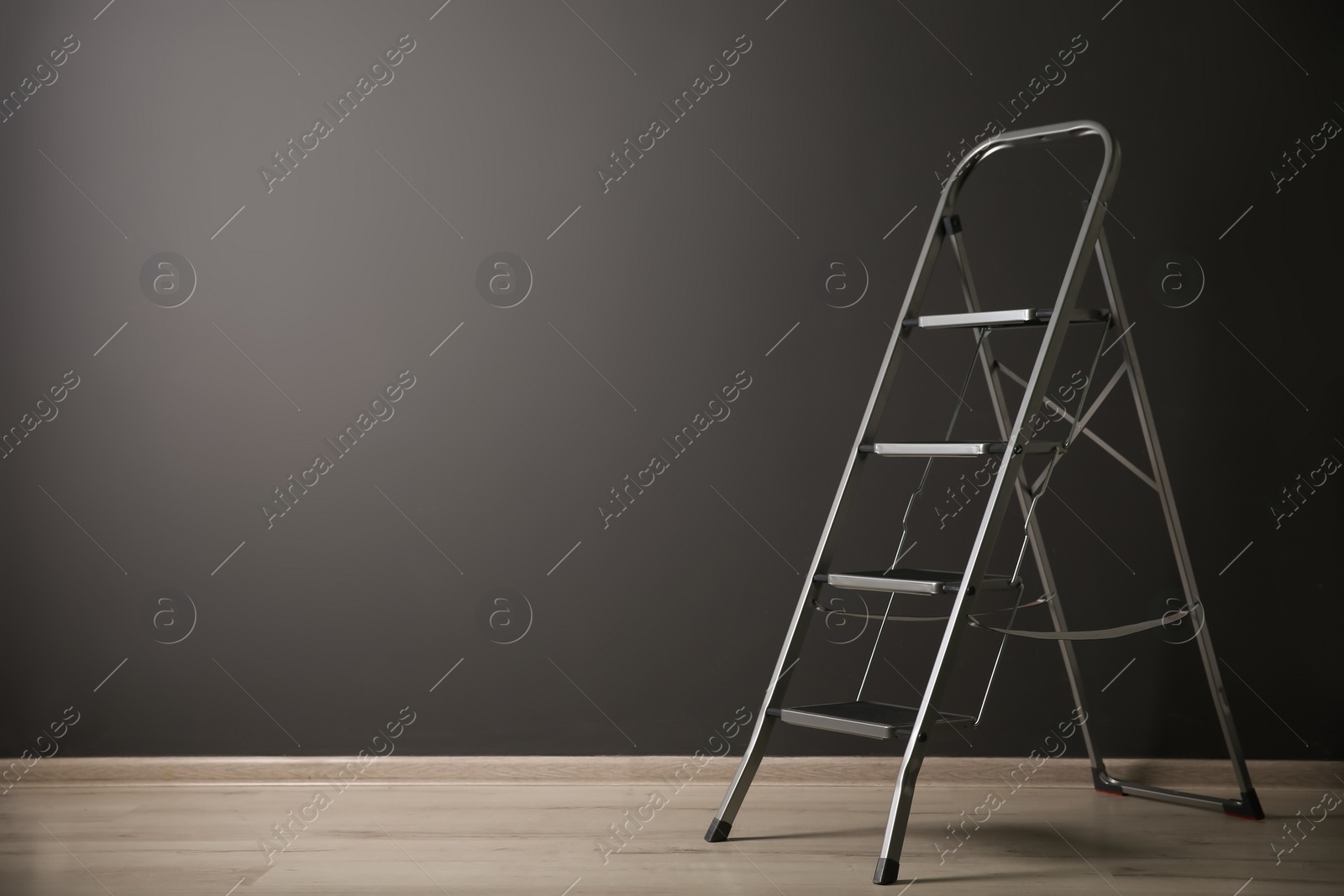 Photo of Modern metal stepladder near grey wall indoors. Space for text