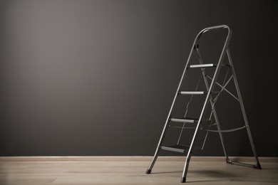 Photo of Modern metal stepladder near grey wall indoors. Space for text