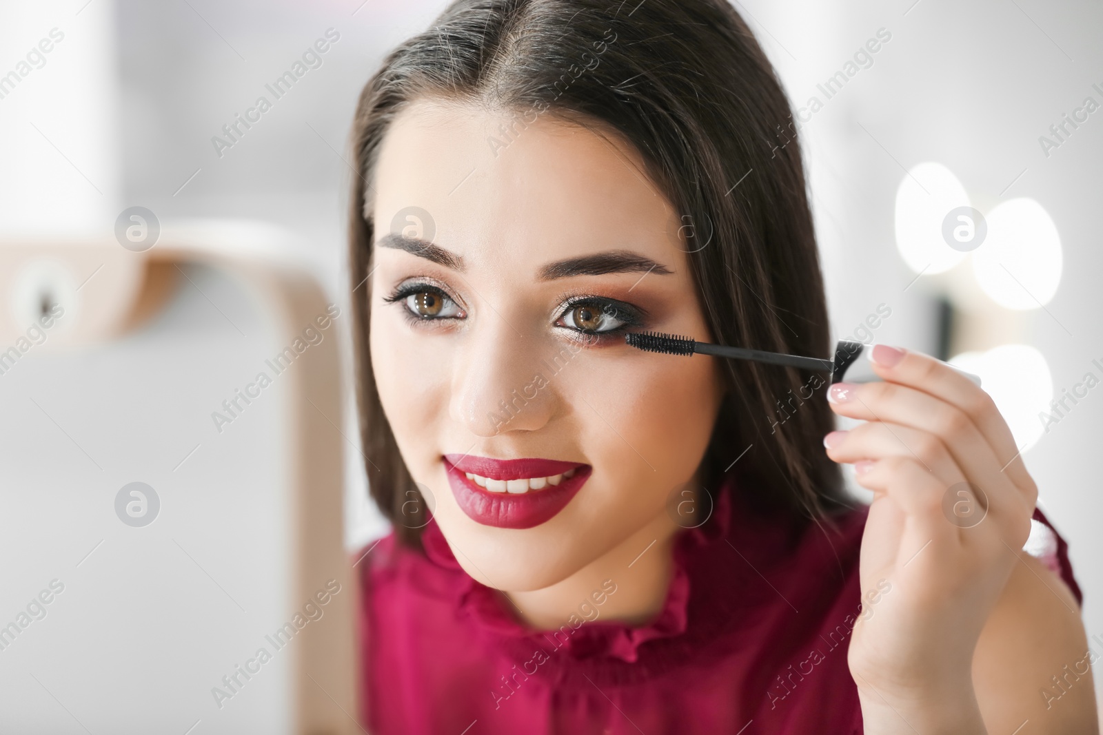 Photo of Portrait of beautiful woman applying makeup on blurred background