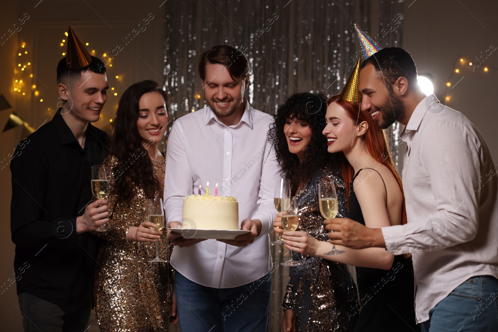 Photo of Happy friends with tasty cake and glasses of sparkling wine celebrating birthday indoors