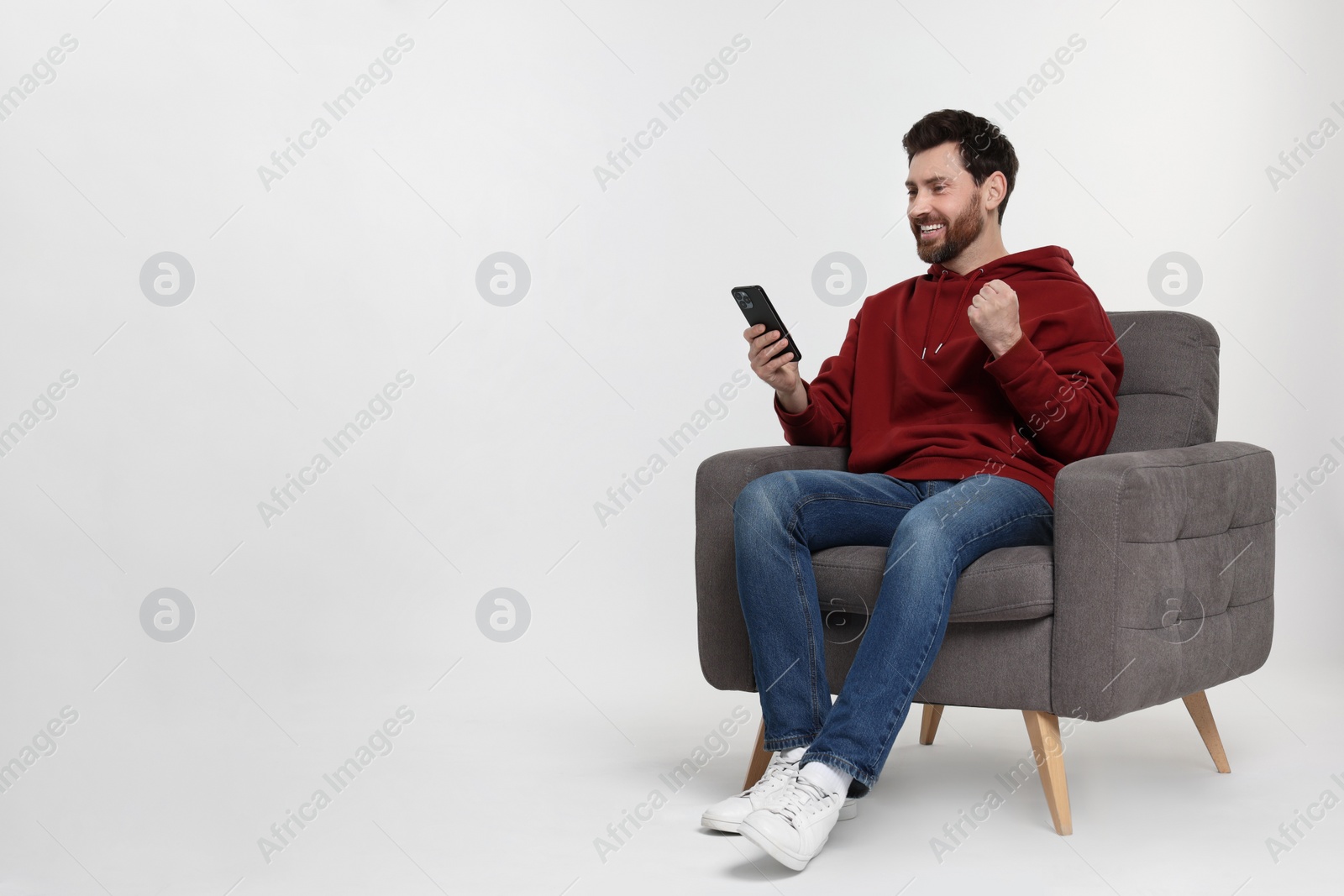 Photo of Happy man with smartphone sitting on armchair against white background. Space for text