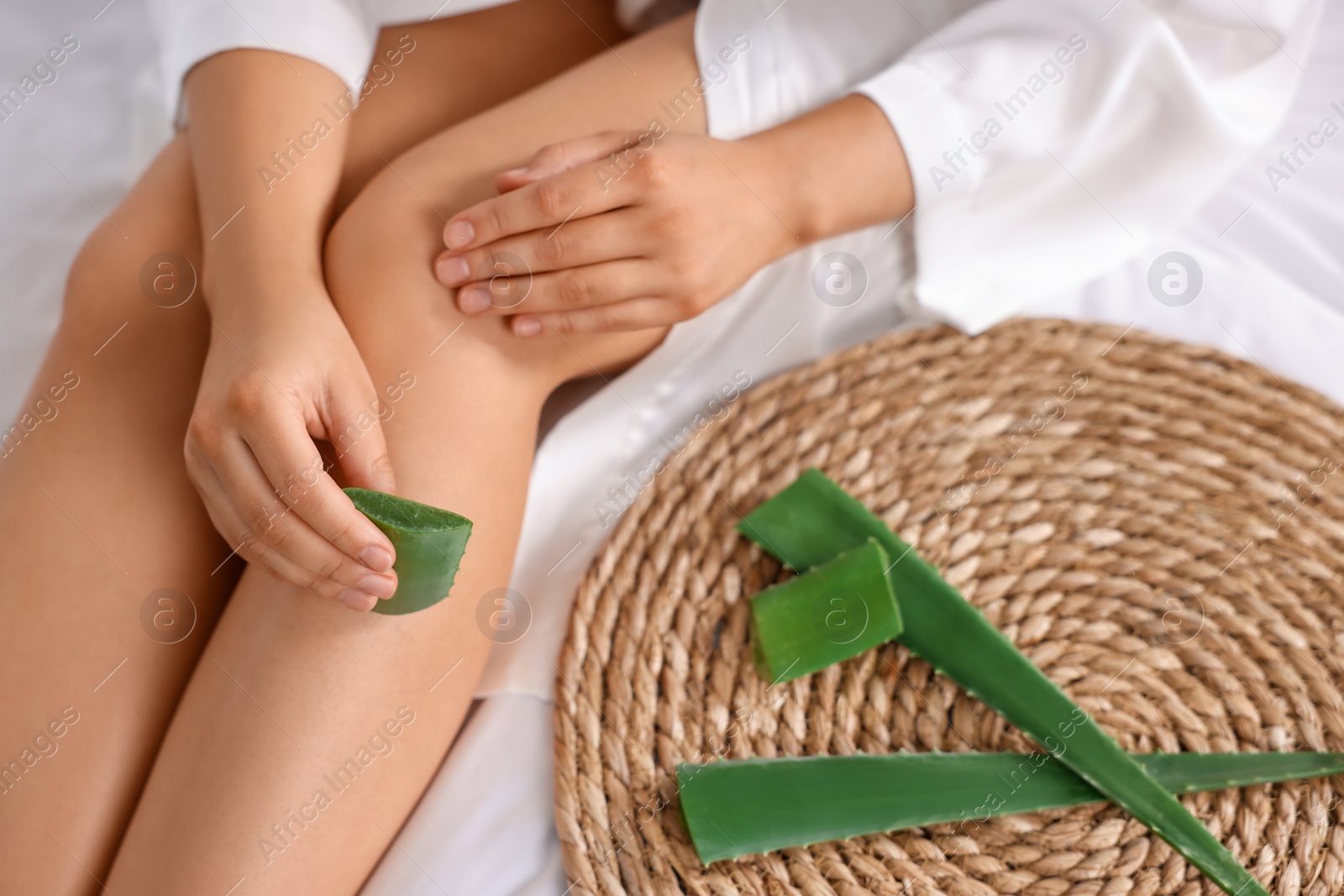 Photo of Young woman applying aloe gel from leaf onto her leg on bed, closeup