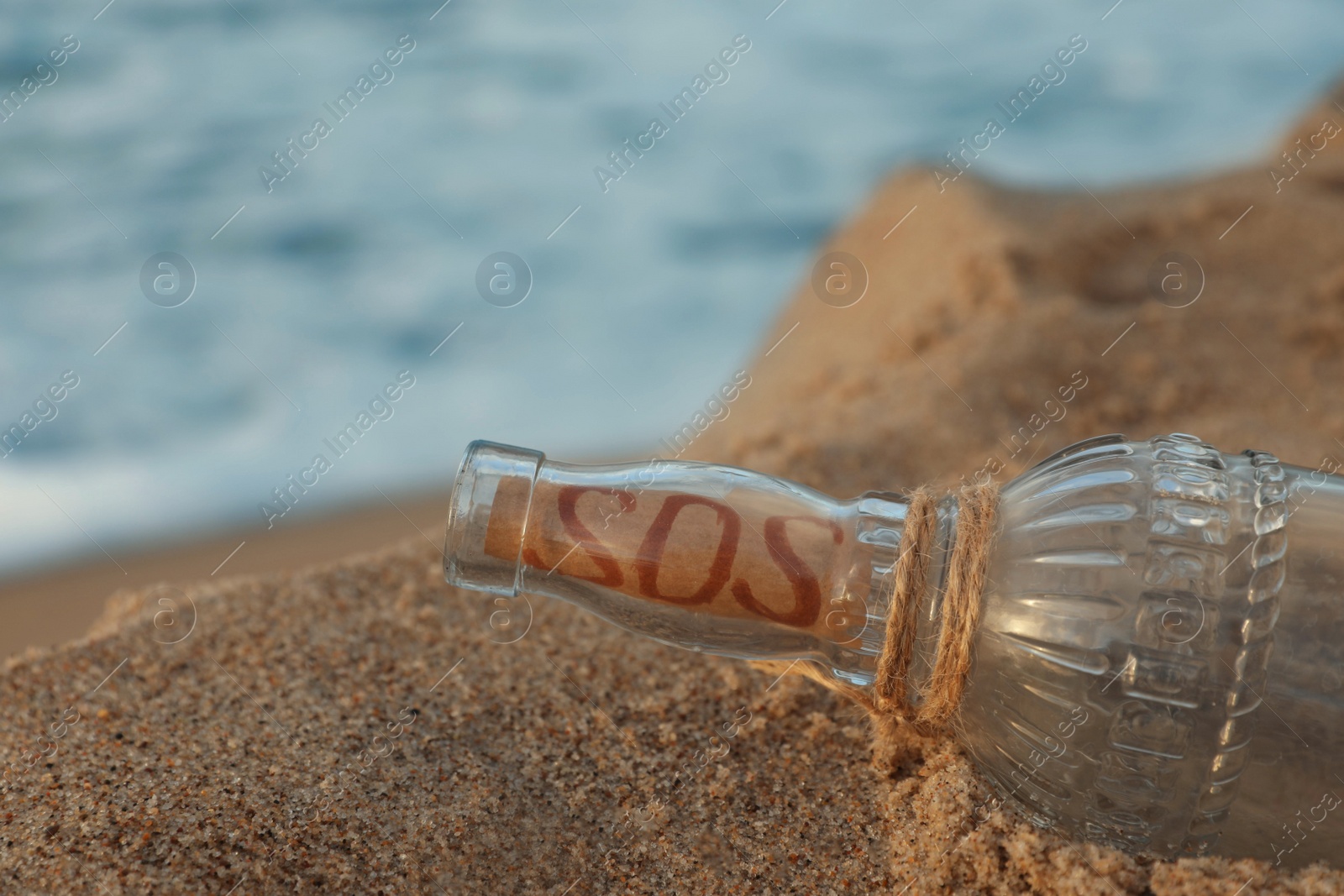 Photo of Glass bottle with SOS message on sand near sea, space for text