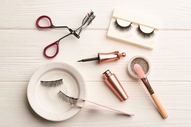 Flat lay composition with magnetic eyelashes and accessories on white wooden table