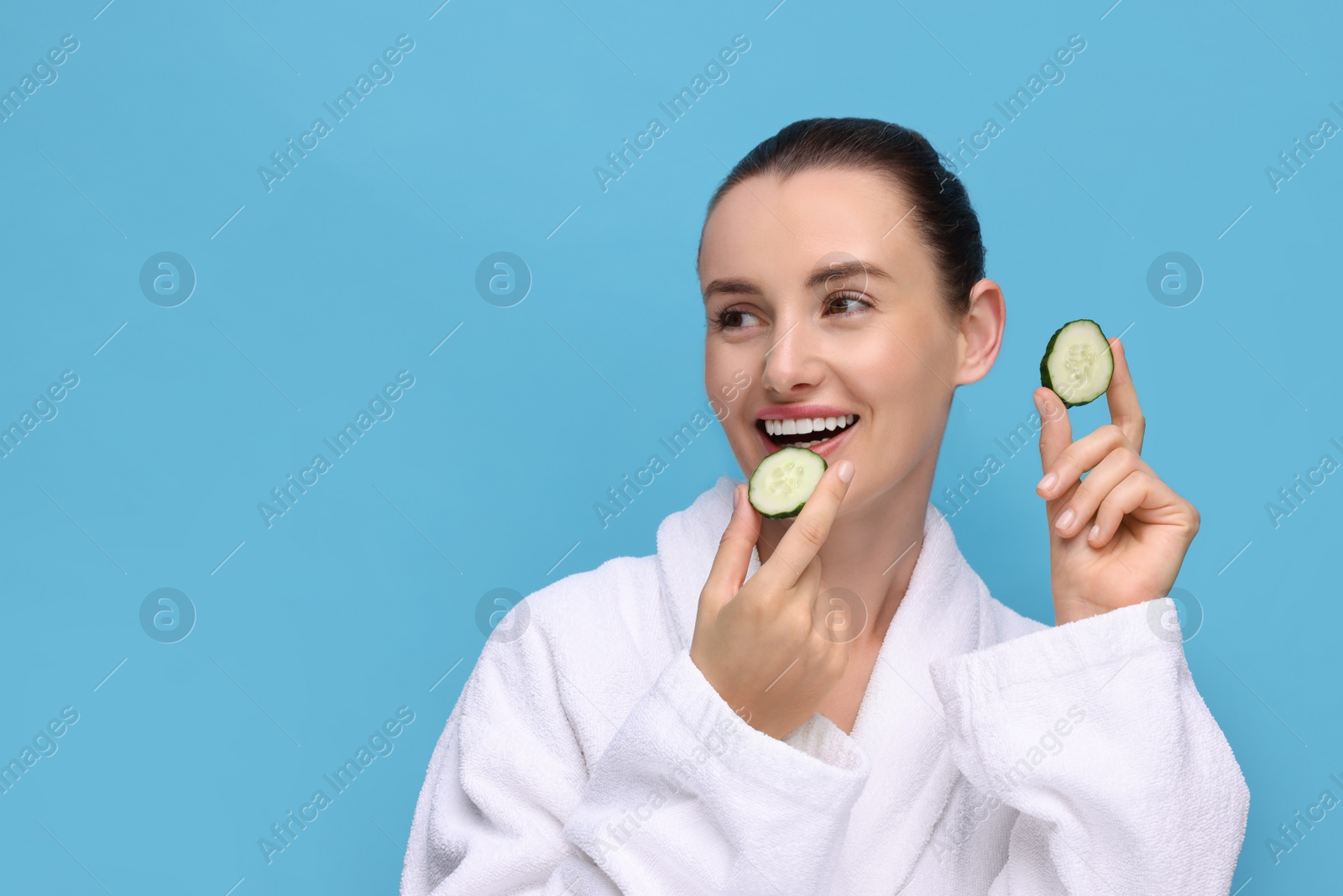 Photo of Beautiful woman with pieces of cucumber on light blue background, space for text