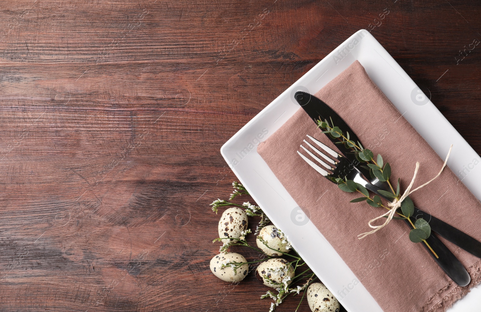 Photo of Festive Easter table setting with quail eggs and floral decor on wooden background, flat lay. Space for text