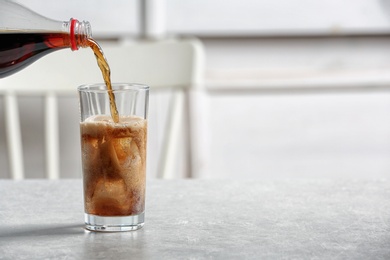 Photo of Pouring cola from bottle into glass on table. Space for text