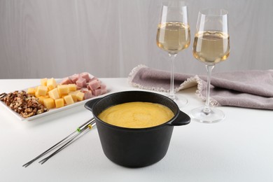 Photo of Fondue with tasty melted cheese, forks, different products and aromatic wine in glasses on white table