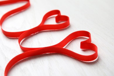 Photo of Hearts made of red ribbon on white wooden background, closeup. Valentine's day celebration