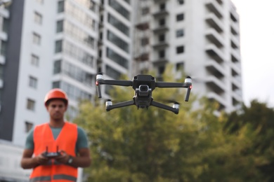 Builder operating drone with remote control at construction site, focus on quadcopter. Aerial survey