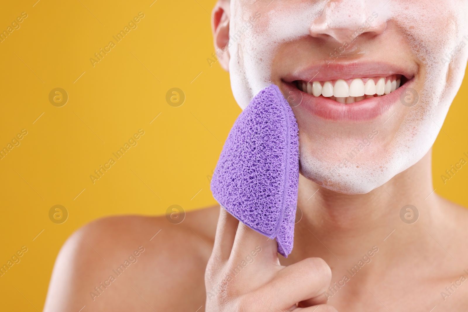 Photo of Happy young man washing his face with sponge on orange background, closeup